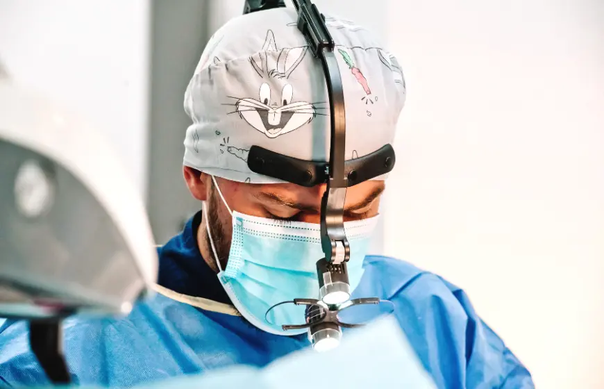 Implantolog Wojciech Skocz z czepkiem chirurgicznym ze śmiesznym królikiem ze znanej kreskówki i lupą chirurgiczną na głowie, przeprowadzający zabieg implantologiczny