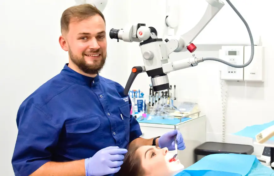 Lekarz dentysta implantolog Wojciech Skocz wykonujący przegląd stomatologiczny pod mikroskopem w PrecisDENT Centrum Implantologii i Stomatologii Mikroskopowej