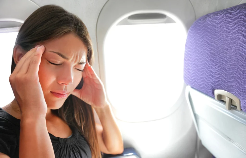 Kobieta trzyma się dłońmi w okolicy stawu skroniowo-żuchwowego i dolnych zębów w trakcie lotu samolotem