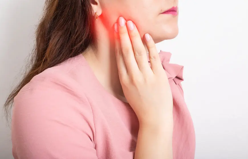 Ból zęba podczas zapalenia kaptura dziąsłowego. Kobieta trzyma się za twarz w okolicy ósemki.