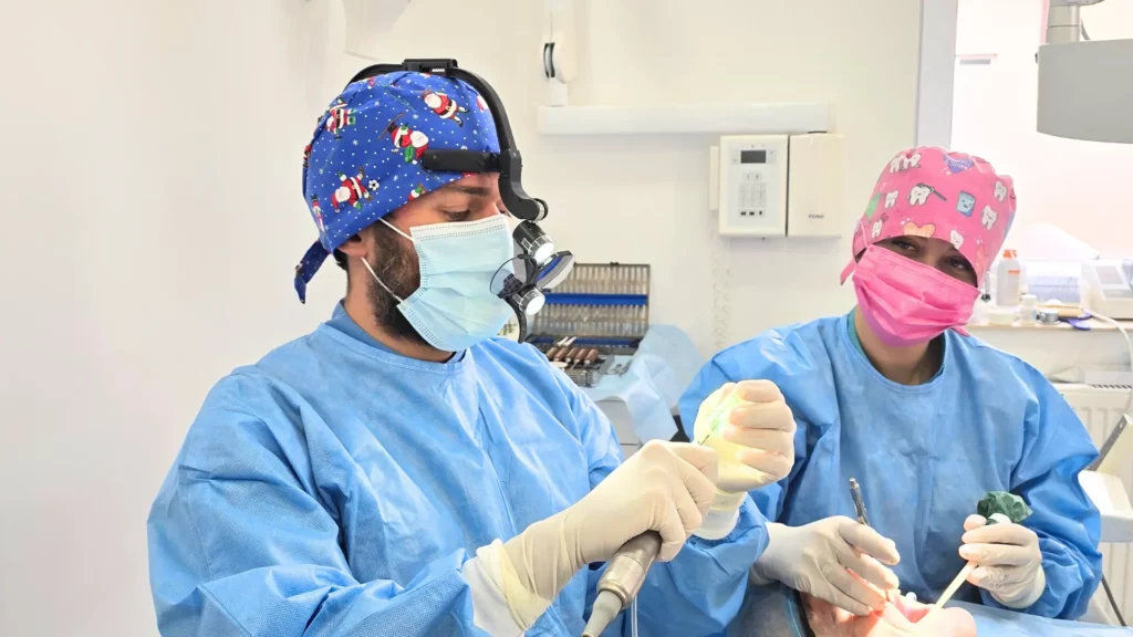 Stomatolog z asystentką stomatologiczną podczas zabiegu wszczepienia implantu cyrkonowego.