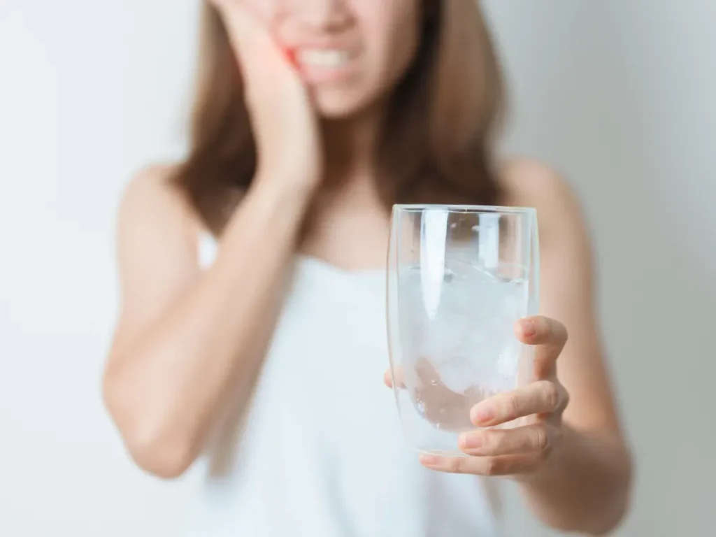 Nadwrażliwość zębiny za zimno i lód. Zdjęcie kobiety trzymającej się za policzek z bólu a w drugiej ręce trzymającej wodę z lodem